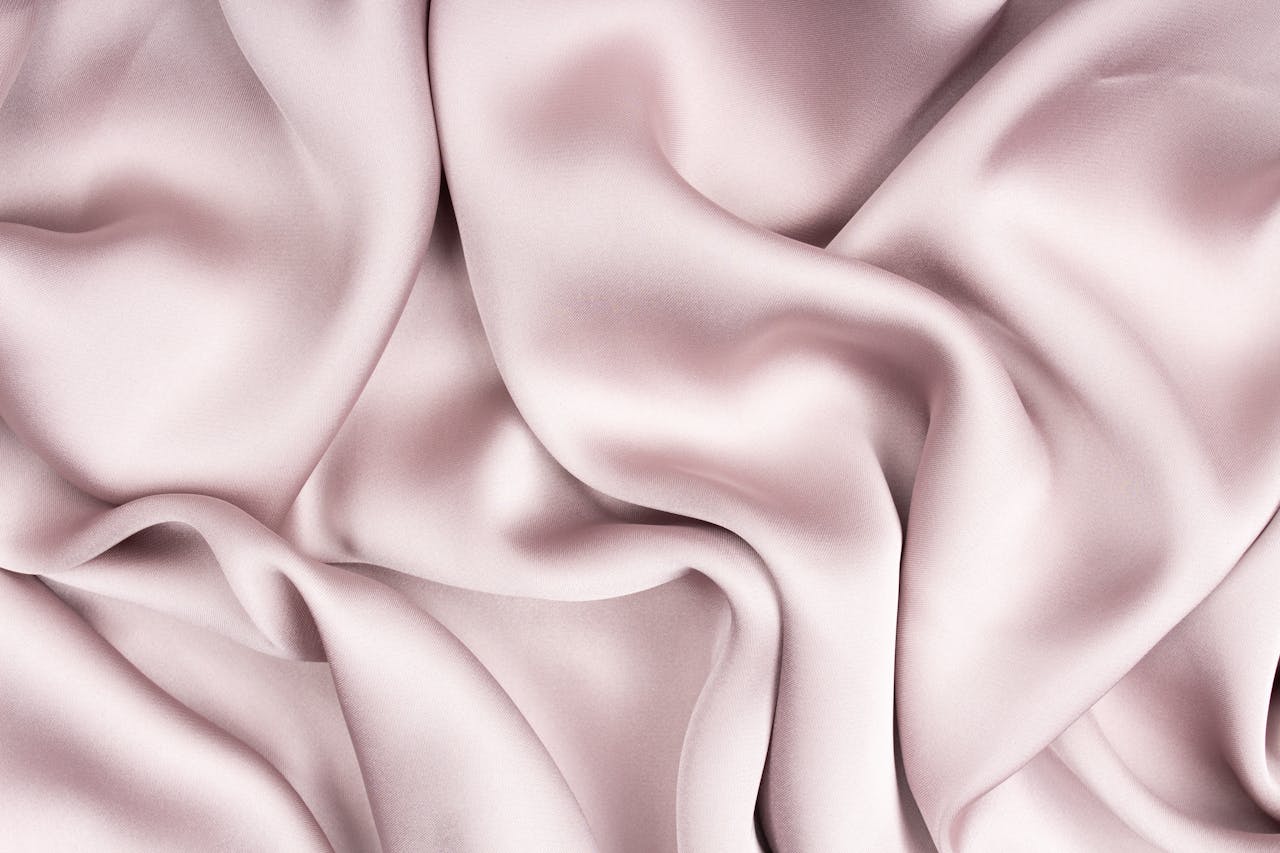 Luxurious close-up of light pink silk fabric with a glossy finish and gentle folds.
